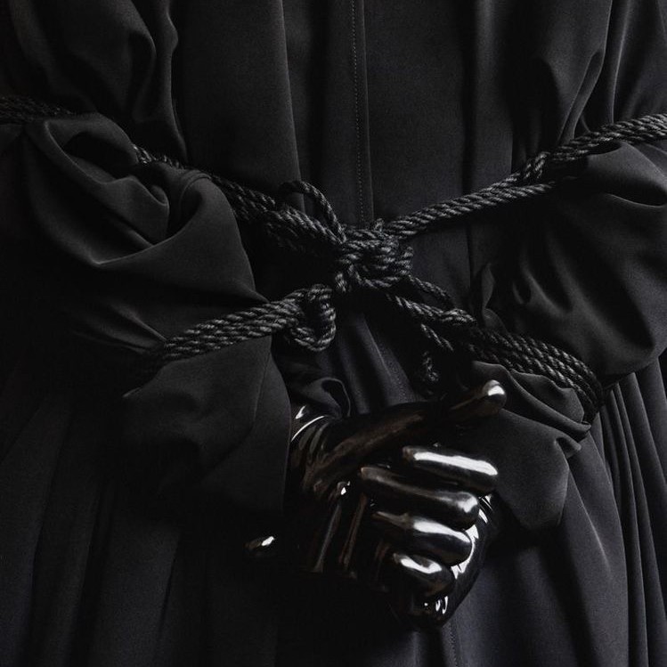 Person from back in black clothing and black gloves, tied up for femdom play